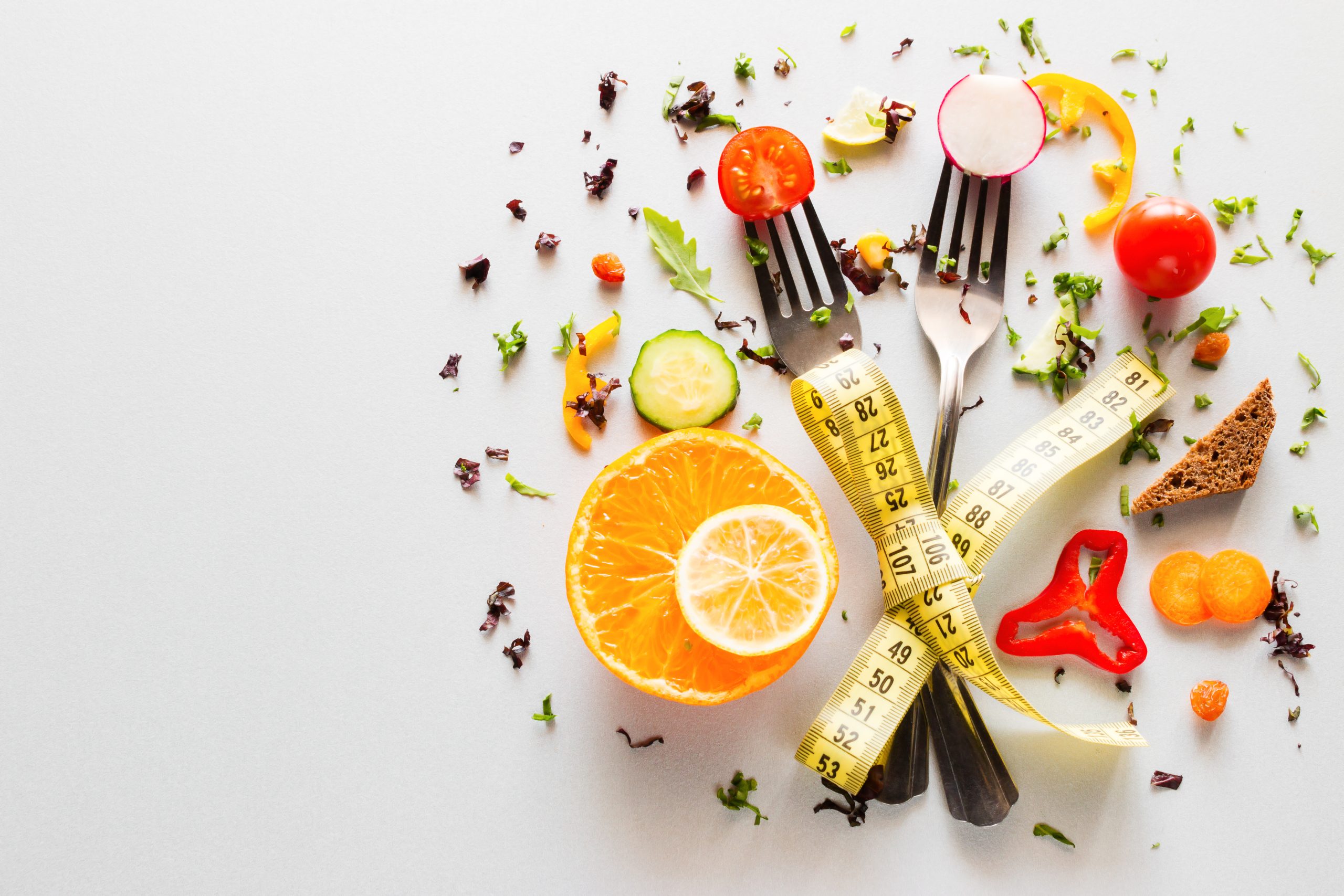 vegetables on forks with measuring tape on a white background with place for text. concept diet, weight loss, fat loss